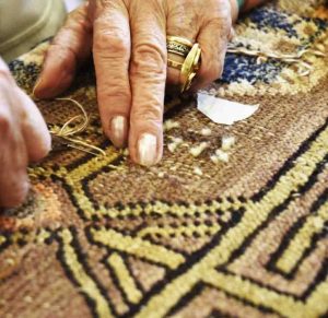 Mani esperte che restaurano le decorazioni di un tappeto annodato a mano