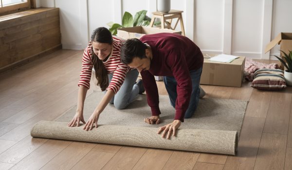giovane coppia che srotola un tappeto moderno grigio in iuta
